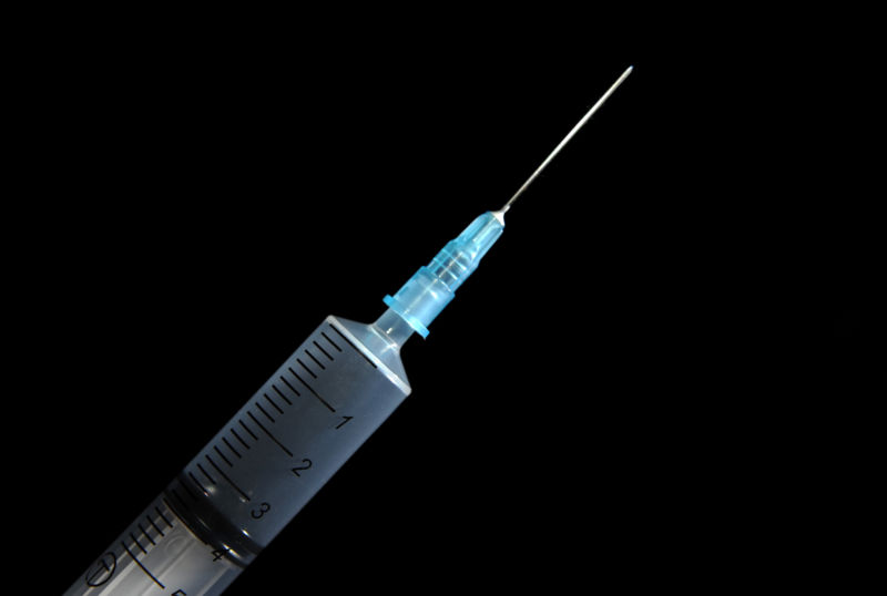 Closeup photograph of hypodermic needle against black background.