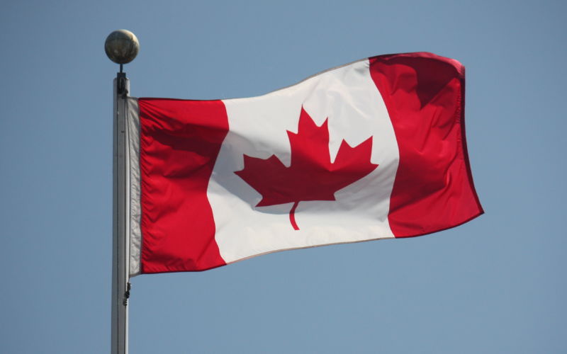 The Canadian flag waves against a blue sky.
