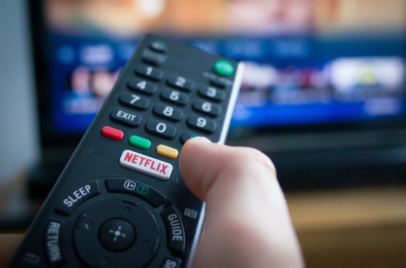 A person's hand holding a TV remote control with a button for Netflix.