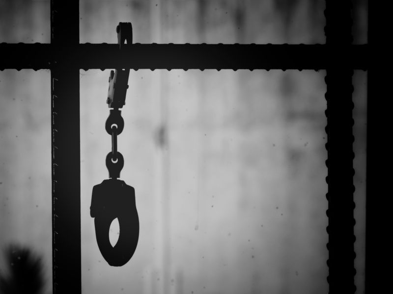 Closeup shot of handcuffs hanging from a metal bar in a prison.