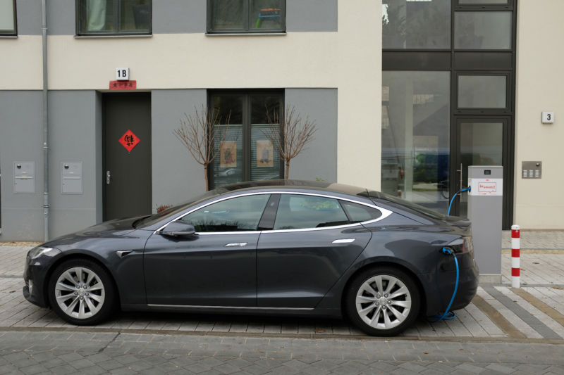 A Tesla sedan on a city street charges at a charging station.